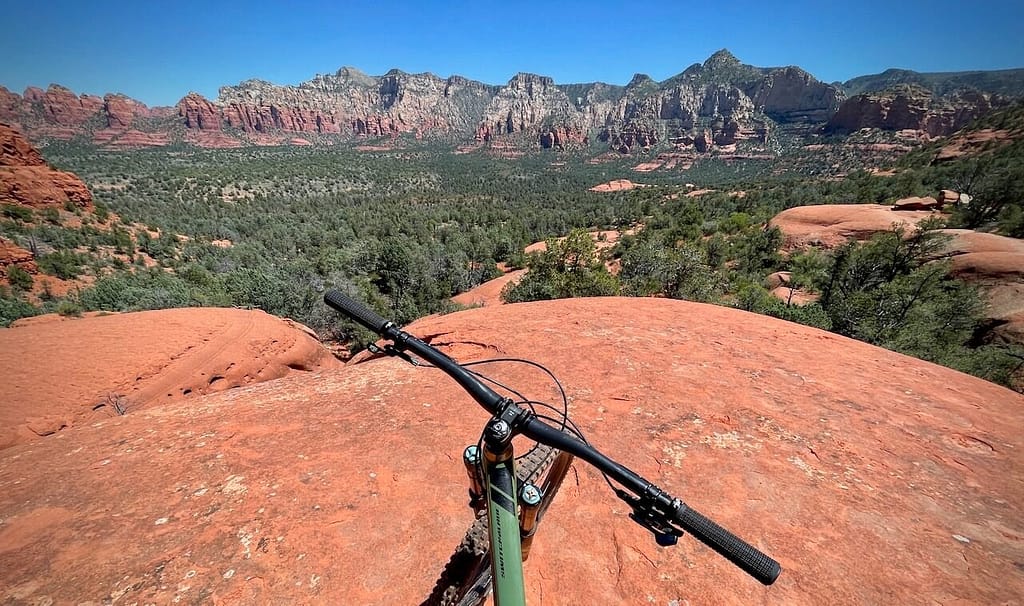 Mountain bike handlebars overlooking Hogs Trail in Sedona Arizona with red rock formations and slickrock terrain. do?
